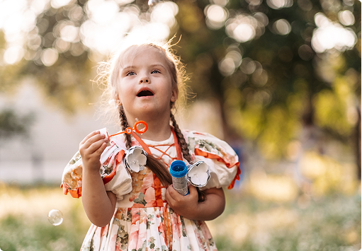 Jeune fille avec des tresses et une robe fleurie, émerveillée en soufflant des bulles de savon dans un parc ensoleillé.